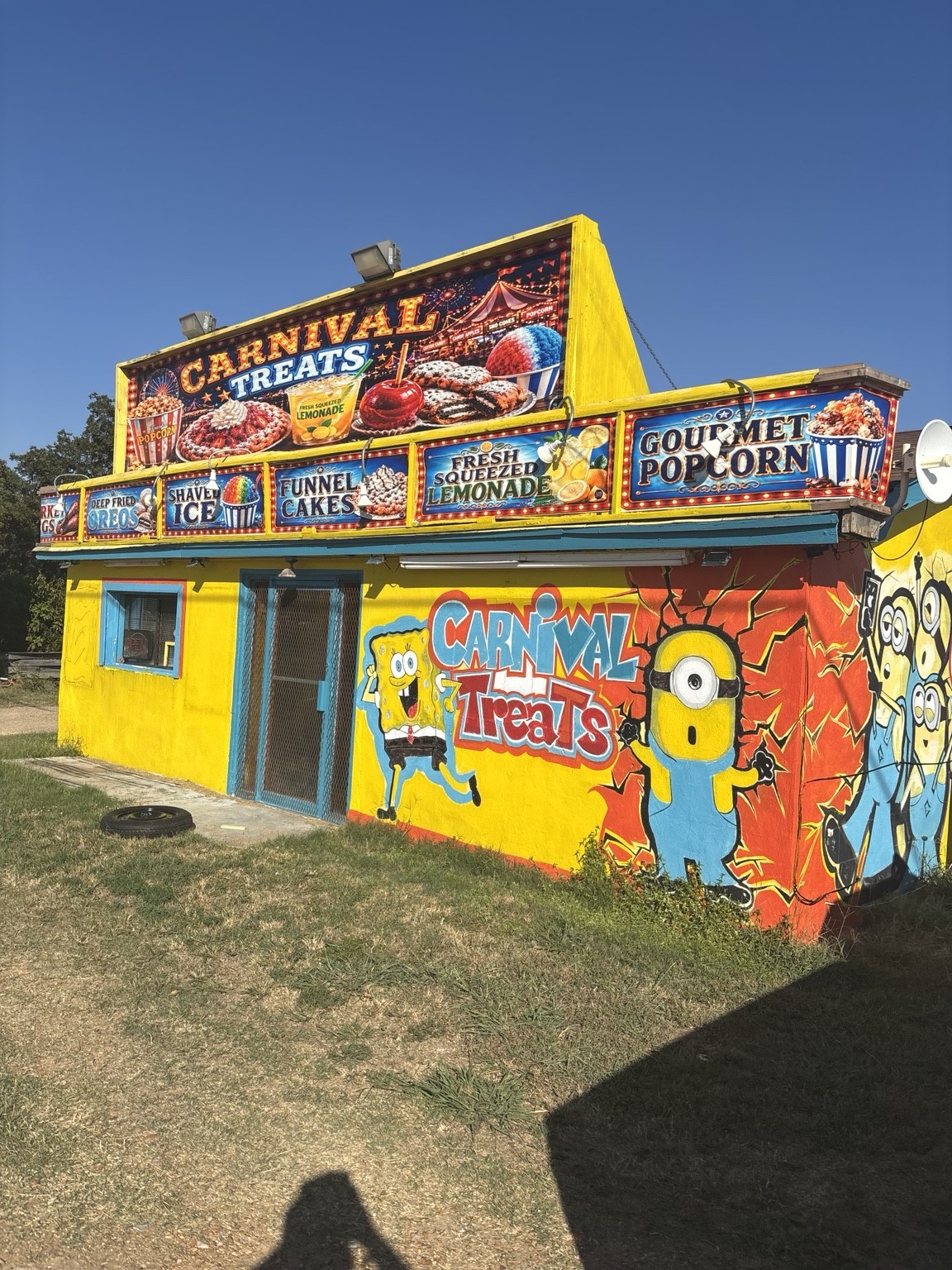 The colorful yellow Carnival Treats building with signs for funnel cakes, lemonade, shaved ice, fried Oreos, and gourmet popcorn